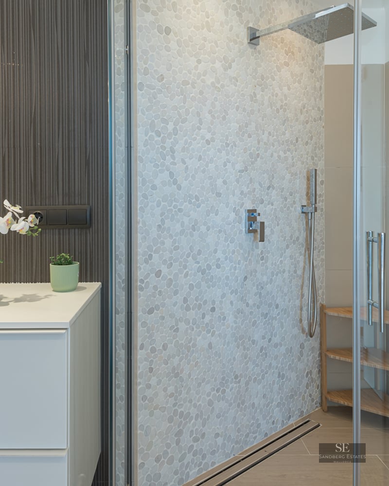 Contemporary bathroom featuring a white vanity and a walk-in glass shower with a textured pebble wall.