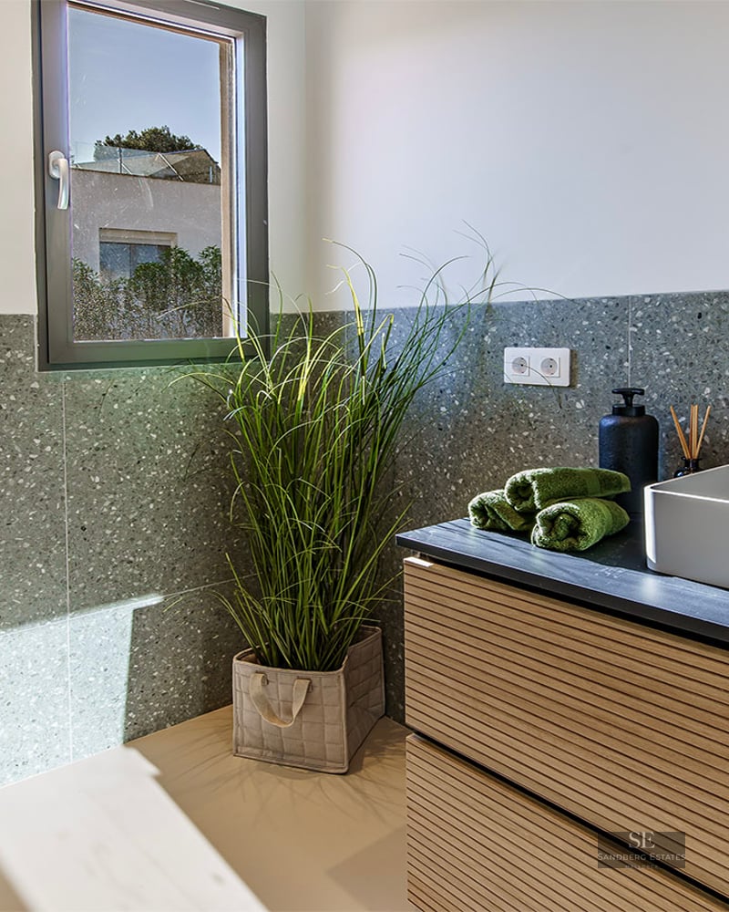 Minimalist bathroom featuring a vessel sink, black faucet, wall-hung toilet, and green terrazzo walls.