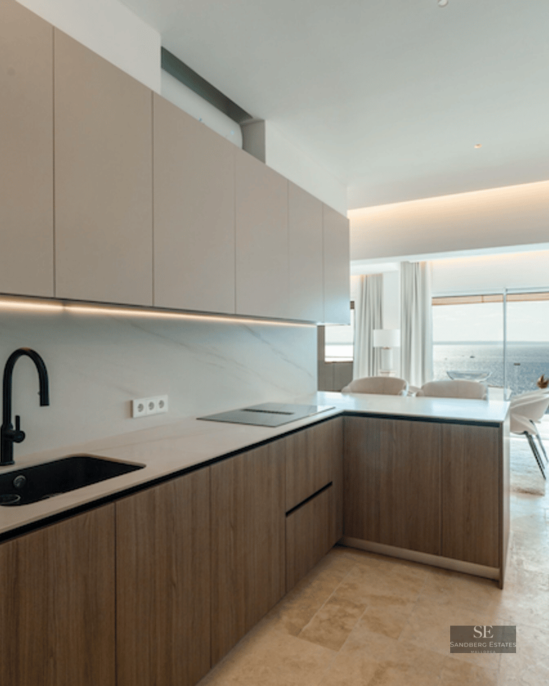 Minimalist kitchen with wood cabinetry, marble backsplash, and a panoramic sea view in the background.