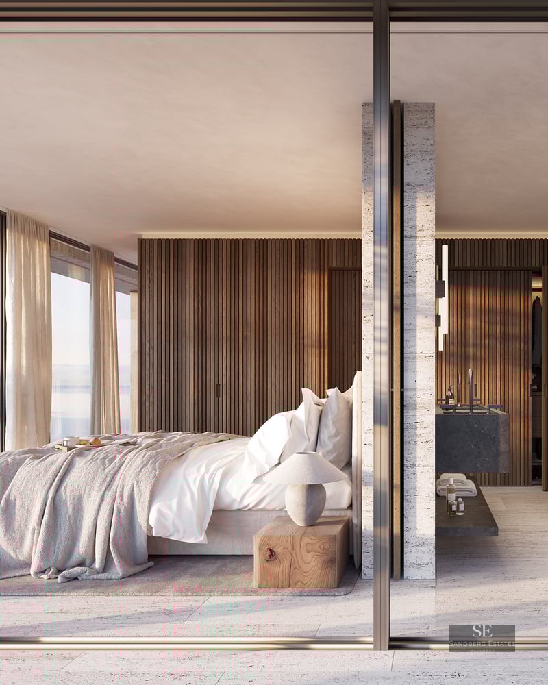 A modern master bedroom and ensuite bathroom separated by glass, featuring a sea view and wood paneling.