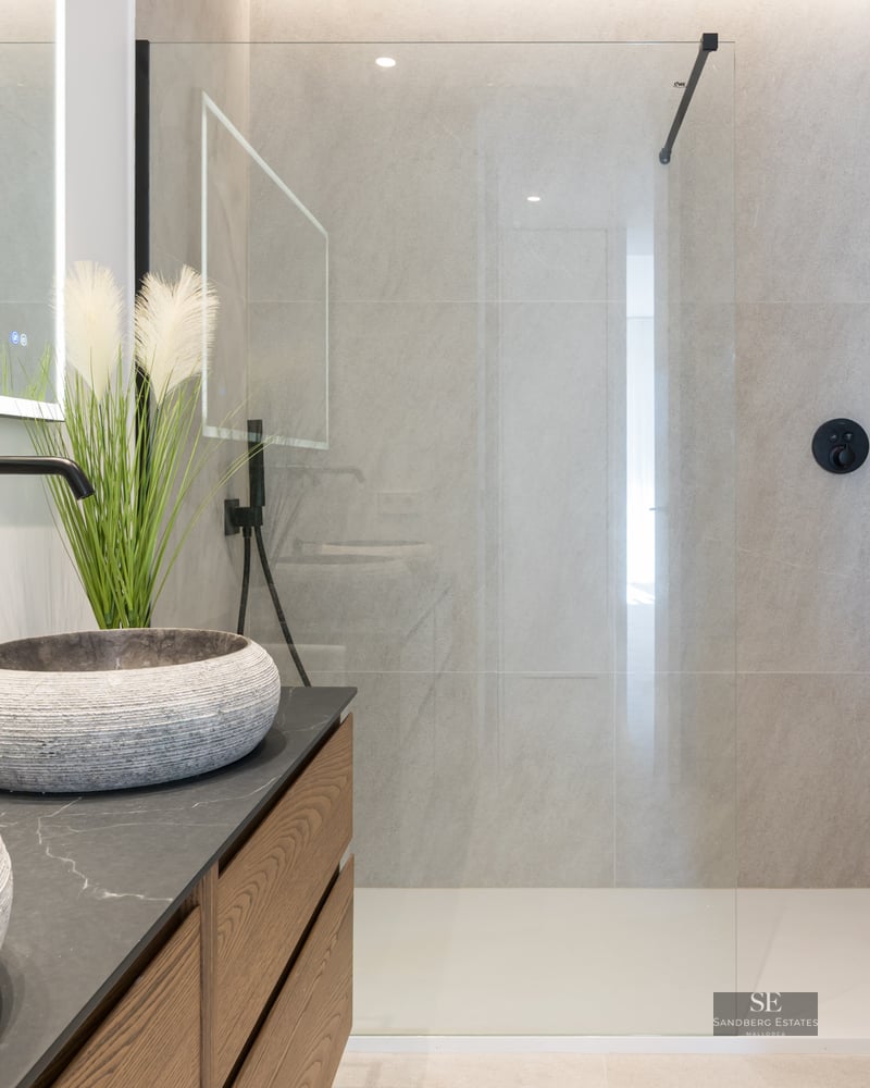 Modern bathroom featuring textured stone bowl sinks, matte black fixtures, and a spacious glass shower enclosure.