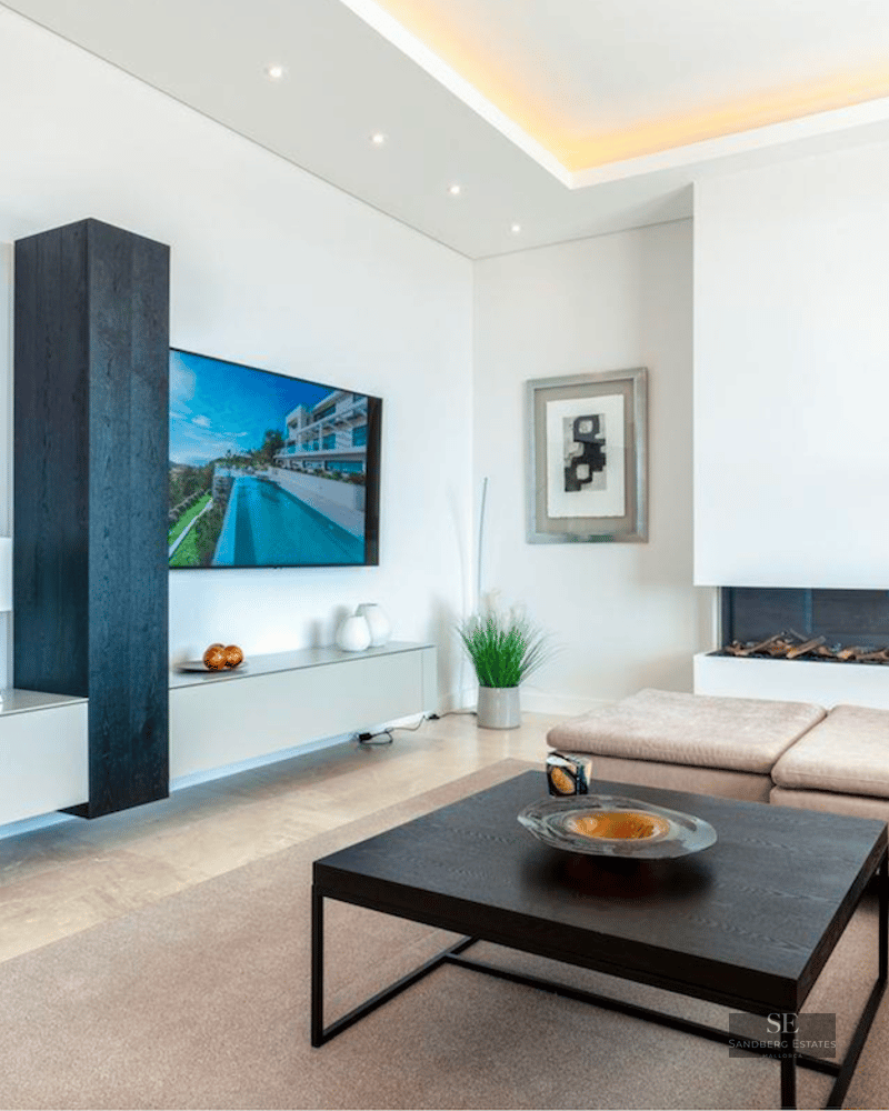 Bright living room featuring a beige sofa, black coffee table, wall-mounted TV, and modern inset fireplace.