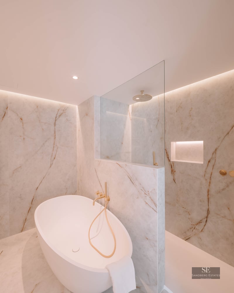 Elegant bathroom featuring a freestanding oval tub, glass shower, and marble walls with gold fixtures.