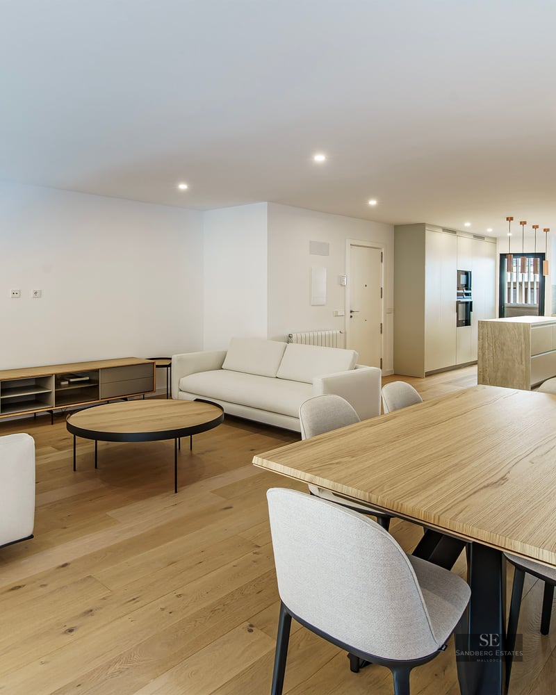 Pièce moderne spacieuse avec canapés blancs, grande table à manger en bois et cuisine contemporaine en arrière-plan.