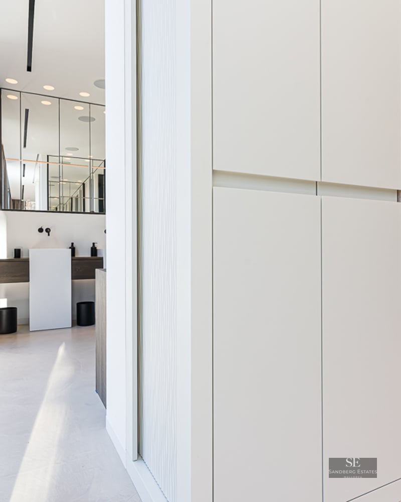 White built-in closets with a cushioned niche leading to a modern bathroom with a pedestal sink.