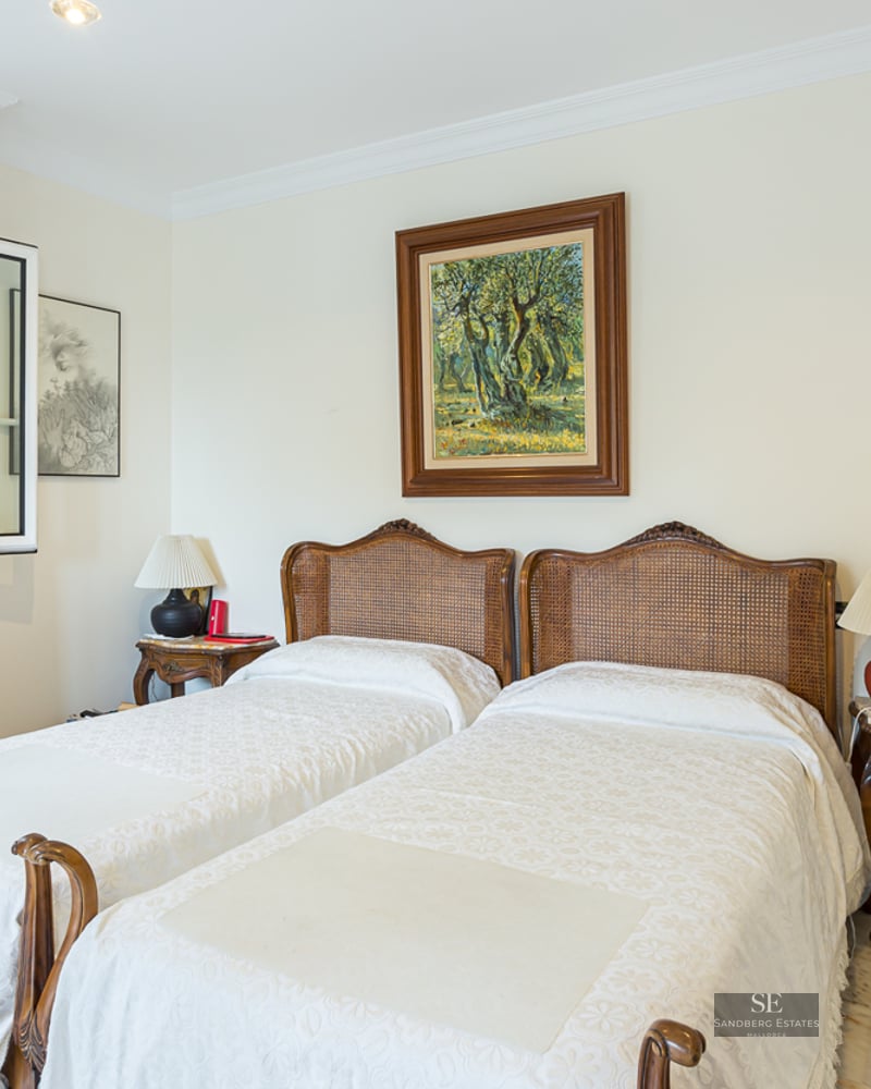 Bedroom featuring two twin beds with wicker headboards, marble flooring, and framed artwork.