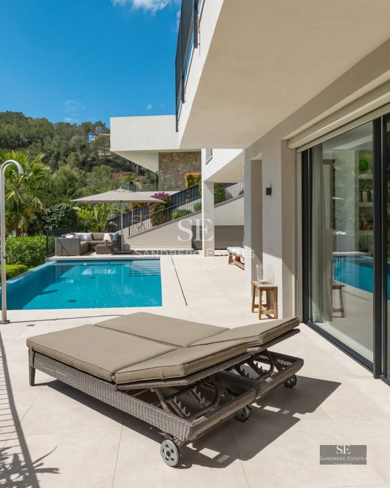 Pool view with wooden terrace, sun loungers, umbrellas and lush garden. Modern design with natural lighting.