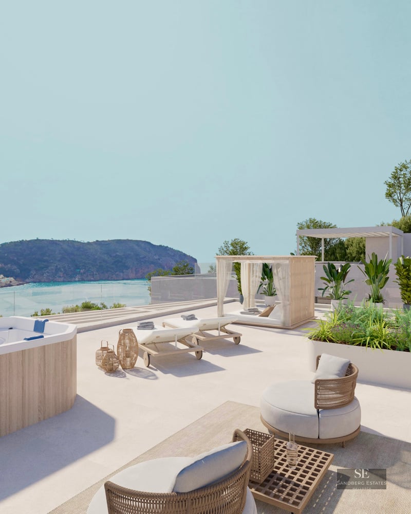 A sunny rooftop terrace with a wood-paneled jacuzzi, sun loungers, and lounge chairs overlooking a coastal bay.