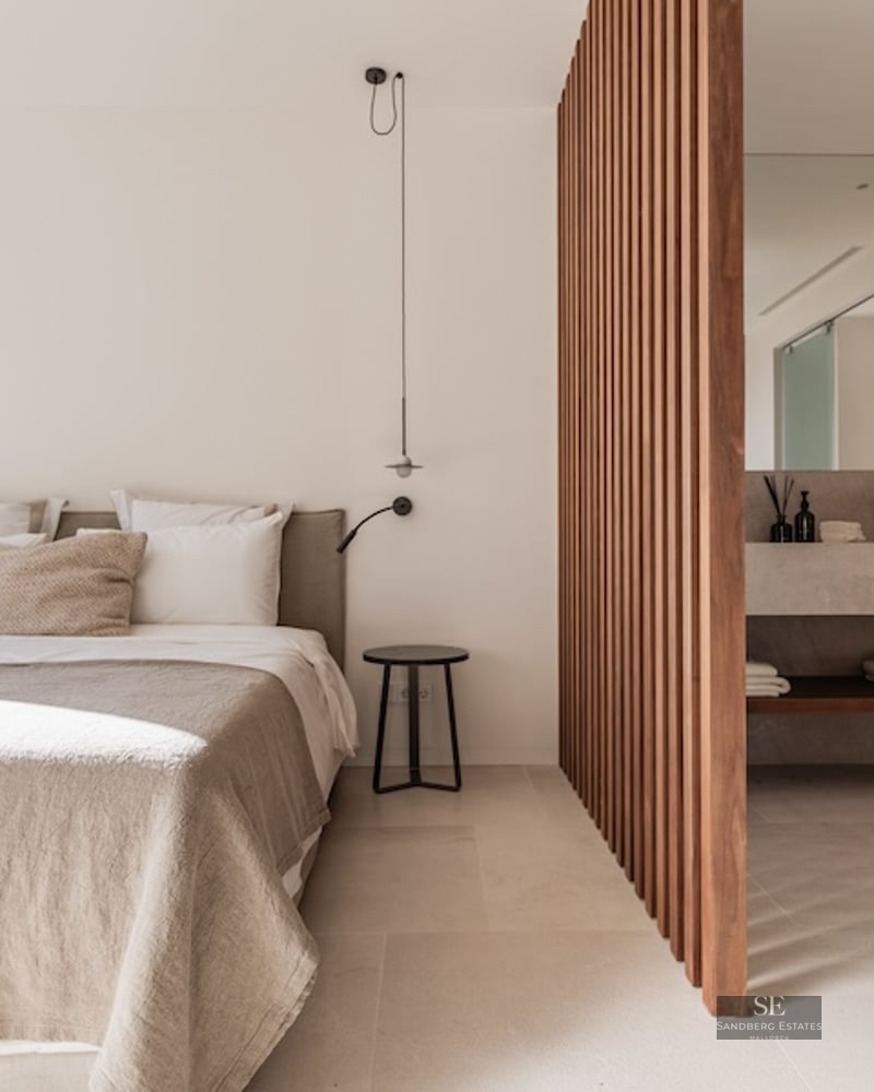 Minimalist beige bedroom separated from a stone vanity by vertical wooden slats.