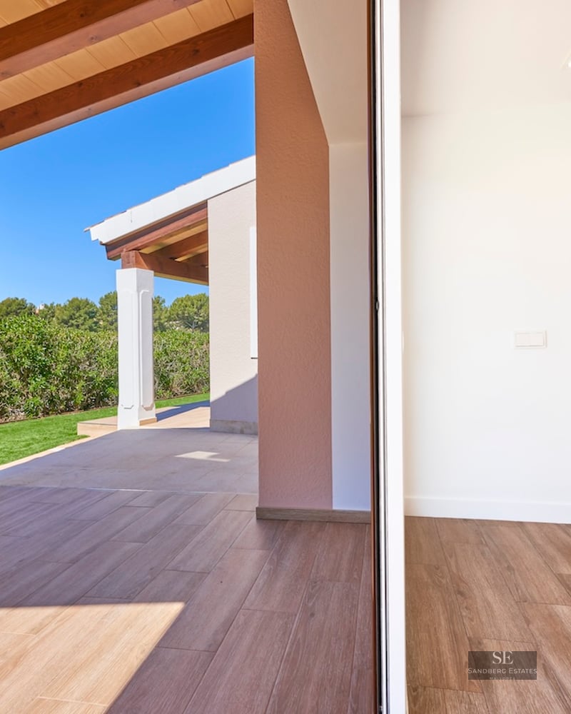 View of a modern terrace with wooden beams and tiled floor connecting to a green lawn under a clear blue sky.