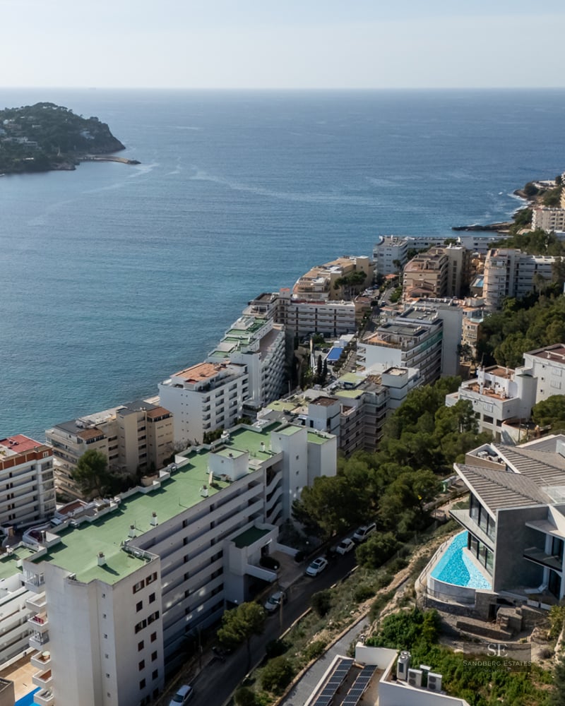 Aerial view of white coastal buildings lining a blue bay and green hills.