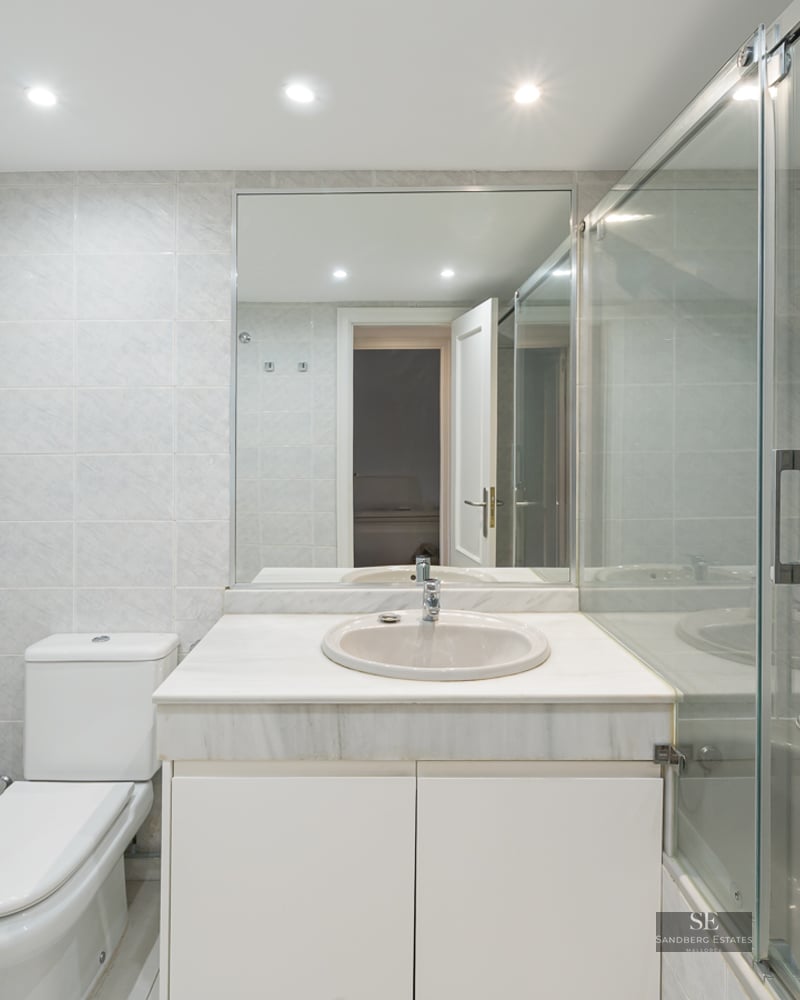 Bright bathroom featuring a white marble vanity, glass shower enclosure, and light grey wall tiles.
