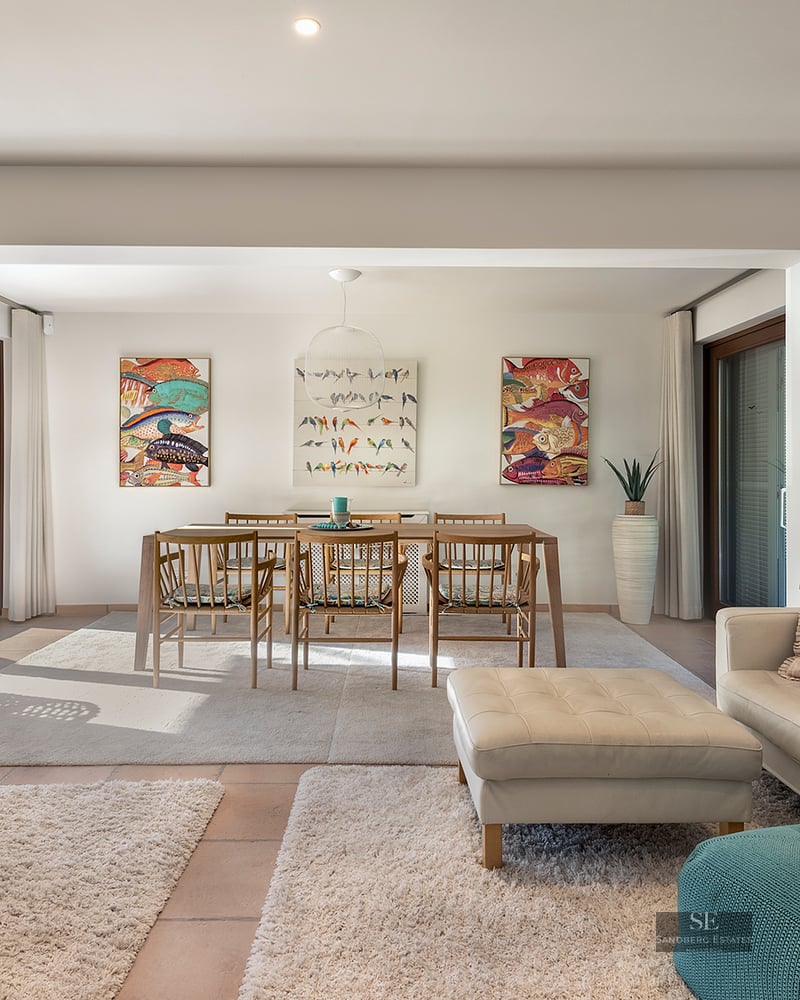 Bright open-plan living room with cream leather sofas, wooden dining table, and colorful fish artwork on white walls.