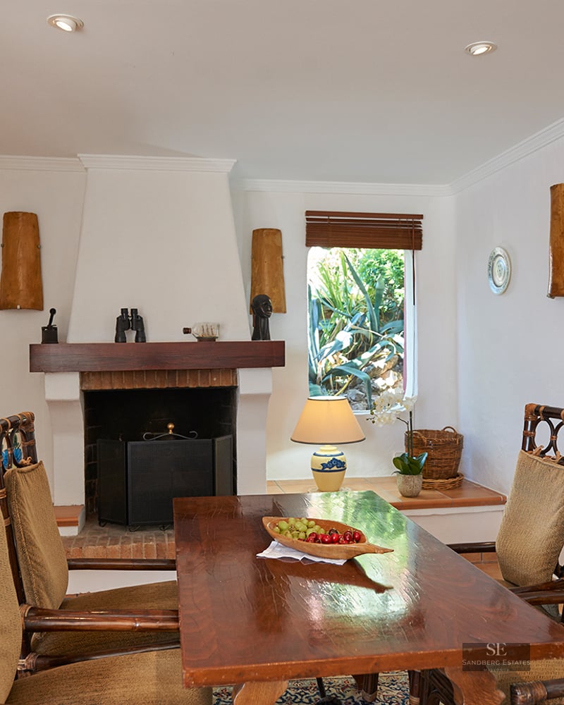 A dining room featuring a wooden table, bamboo chairs, a white fireplace, and decorative wall plates.