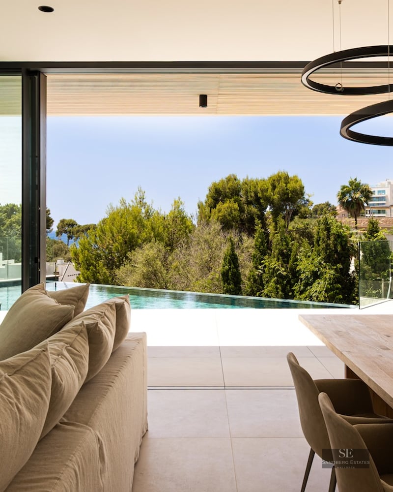 Modern open-plan living and dining area with floor-to-ceiling glass doors opening to an infinity pool and green hills.