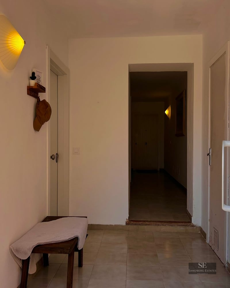 A clean white hallway with a wooden bench, tiled floor, and a glowing fan-shaped wall light near multiple white doors.