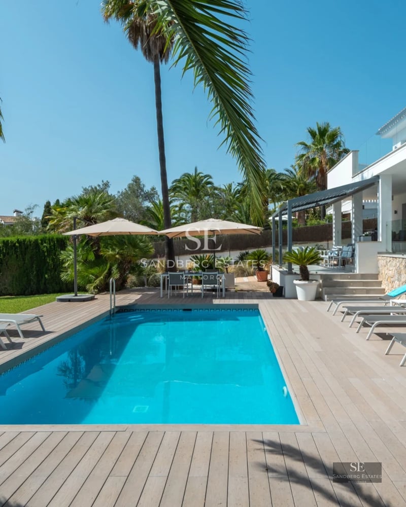Wide view of bright living room with infinity pool and modern furniture. Large windows and lush garden.
