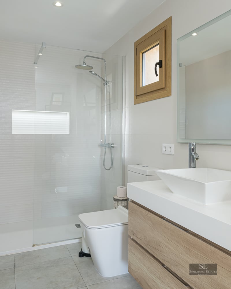 Modern bathroom featuring a walk-in glass shower, wooden vanity with square sink, and chrome heated towel rail.