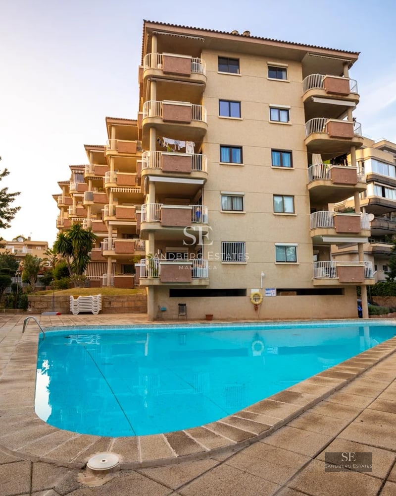 Vue de la piscine à débordement avec des chaises longues, entourée de pelouse et d'une villa moderne avec de grandes baies vitrées. Paysage luxuriant en arrière-plan.