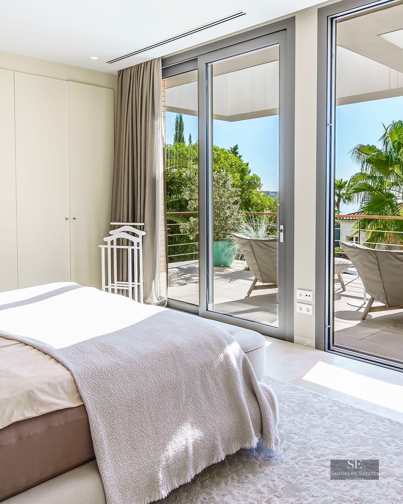 Chambre moderne avec baies vitrées donnant sur une terrasse ensoleillée et des palmiers.