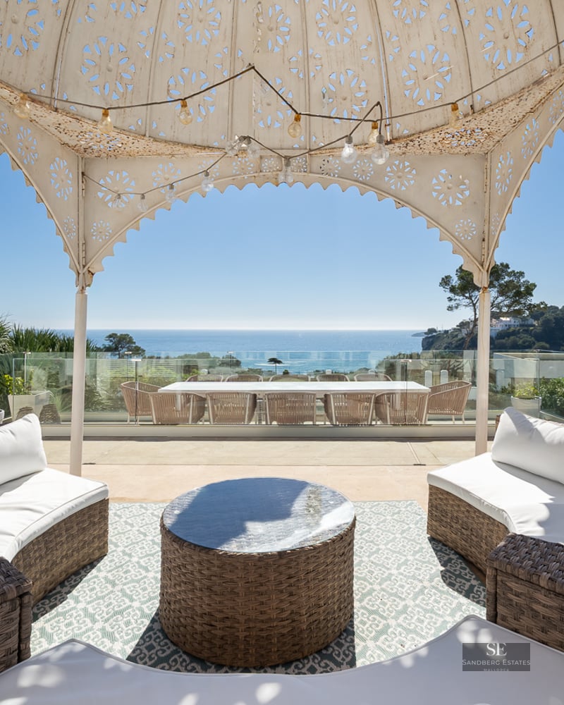 Spacious terrace with wicker sofas under a decorative gazebo overlooking the Mediterranean sea.