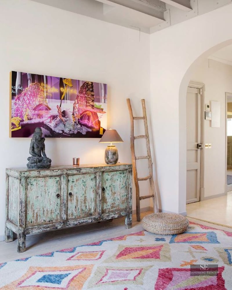 Interior hallway featuring a colorful geometric rug, vintage turquoise sideboard, rustic ladder, and arched stone windows.