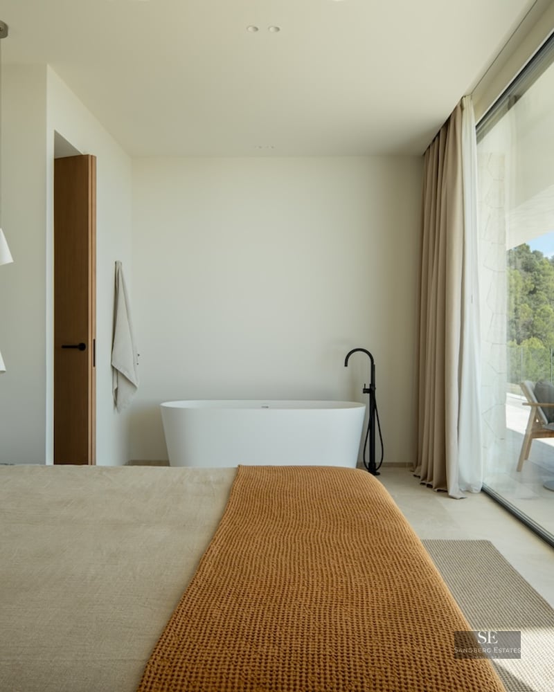 Luxury bedroom with a freestanding bathtub next to large glass doors overlooking a forest and private terrace.