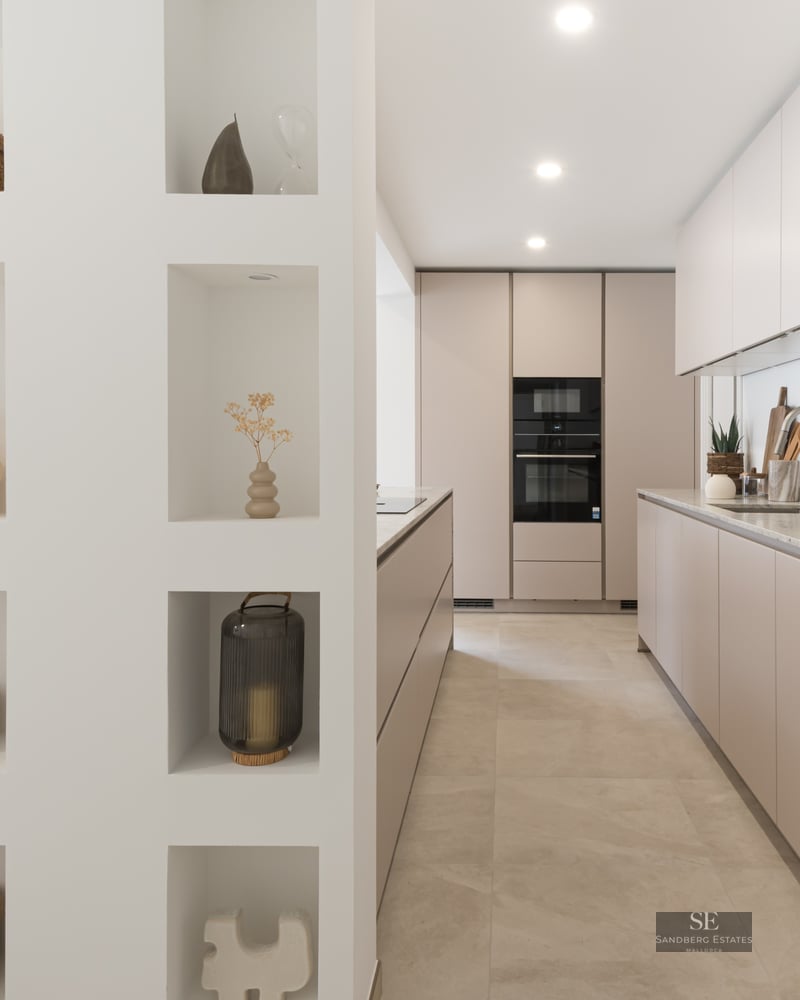 Modern galley kitchen with taupe cabinets next to a white partition wall with eight decorative recessed niches.