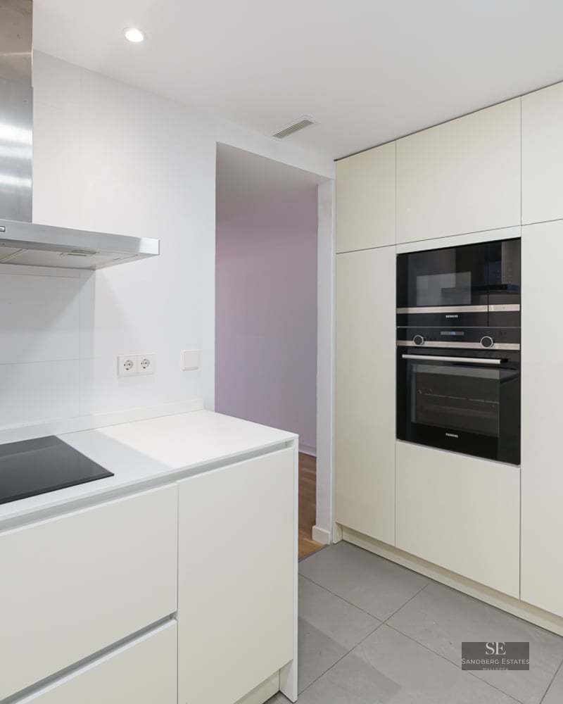 Minimalist white kitchen featuring a stainless steel hood, built-in oven, and a modern black refrigerator.