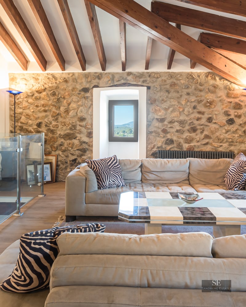 Living room featuring large sofas, exposed stone walls, wooden ceiling beams, and a glass mezzanine railing.