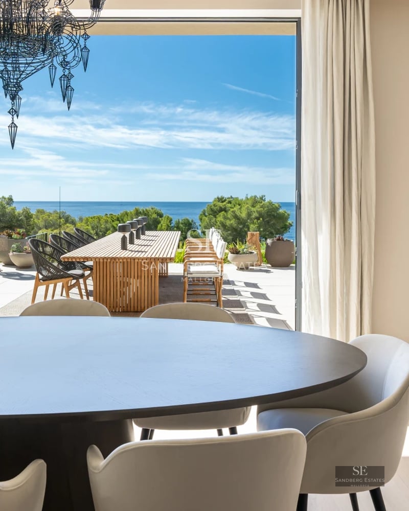 View of poolside garden surrounded by lawn, sun loungers, and a modern house with large windows. Clear sky.