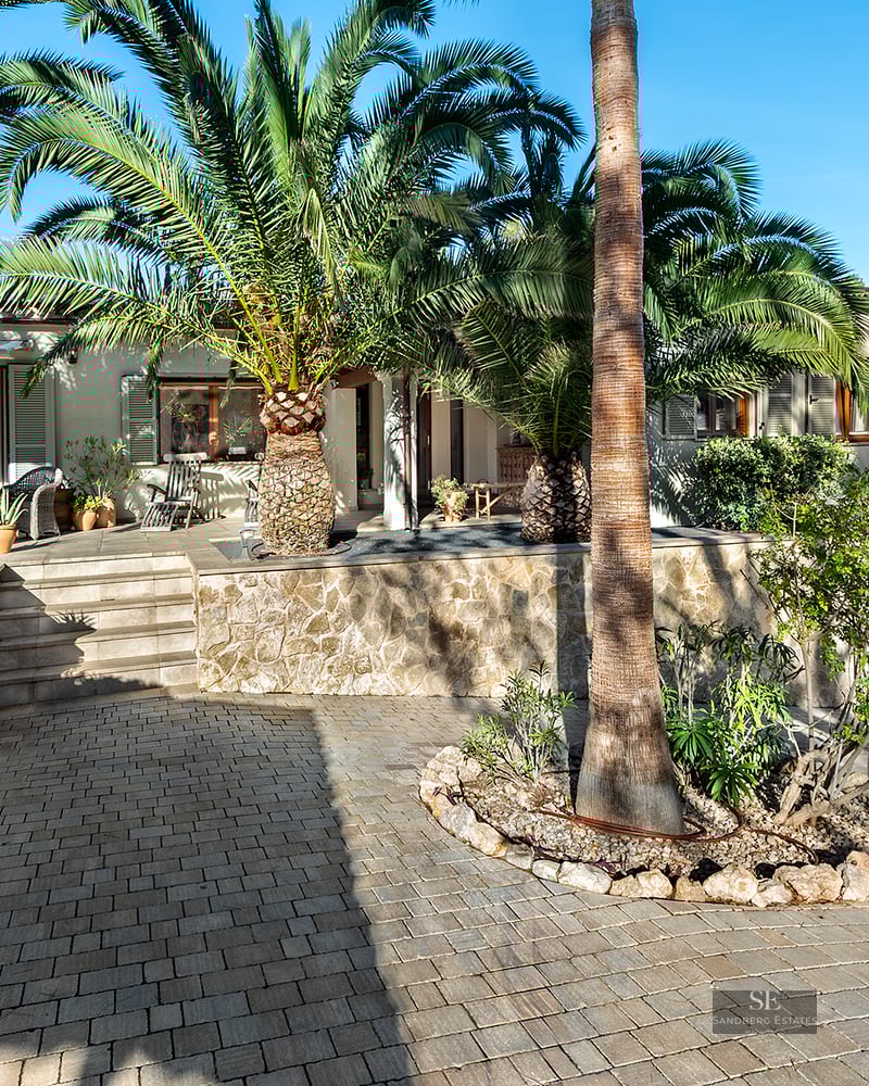 Exterior of a Mediterranean house with stone walls and large palm trees under a clear blue sky.