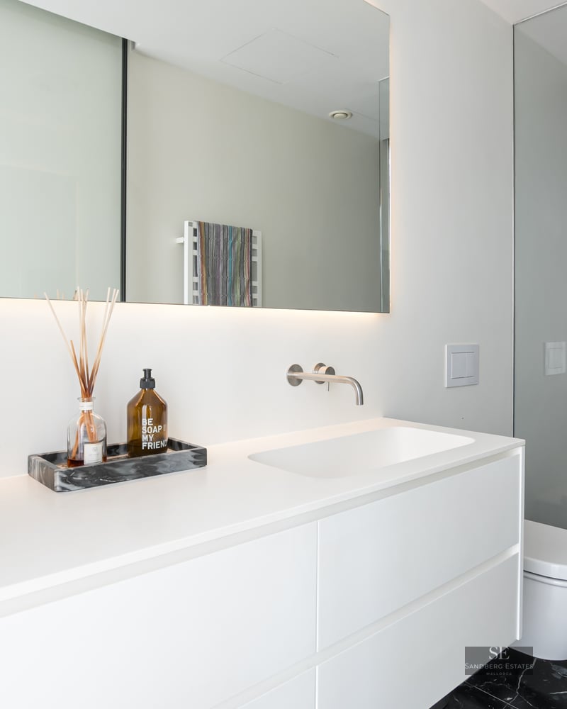Minimalist white bathroom featuring a floating vanity and a walk-in shower with luxurious black marble walls.