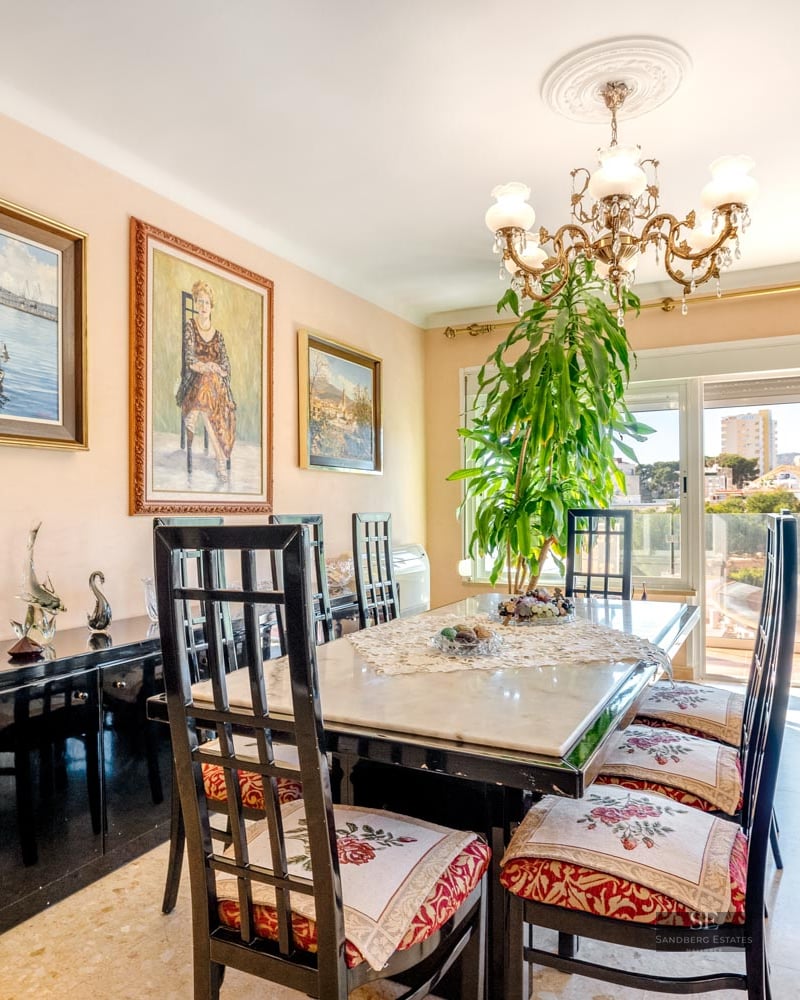 Traditional dining room with a marble table, high-backed chairs, a chandelier, and large glass doors with a city view.