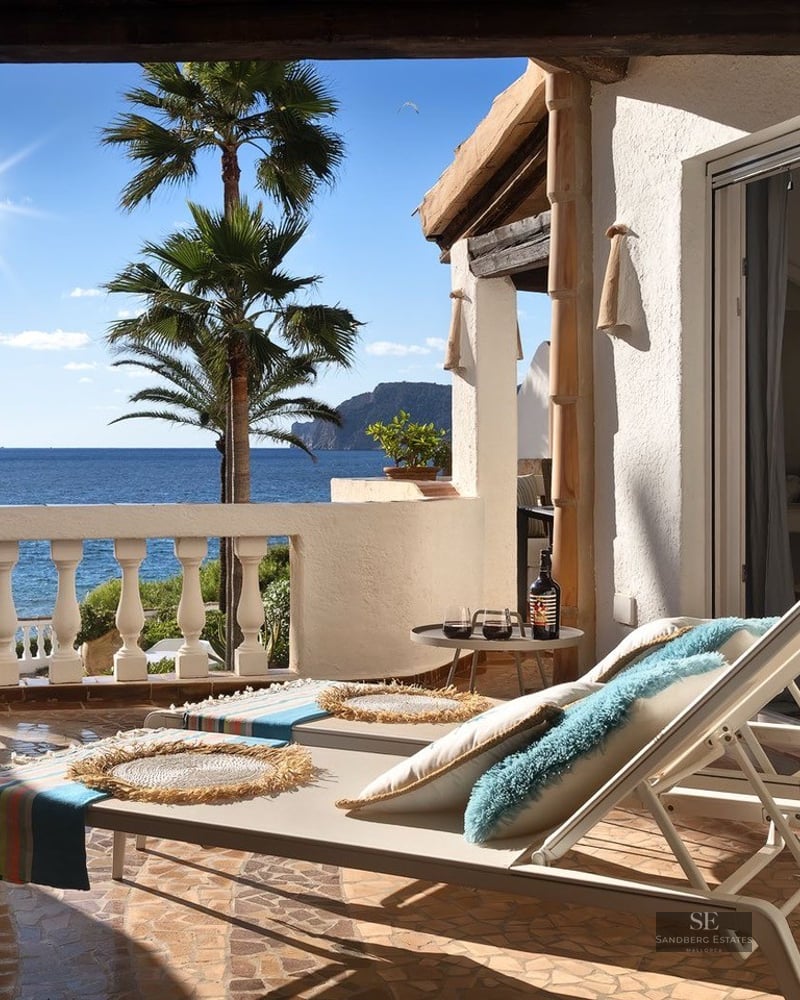 White sun loungers on a Mediterranean terrace overlooking the ocean with palm trees under a bright sun.