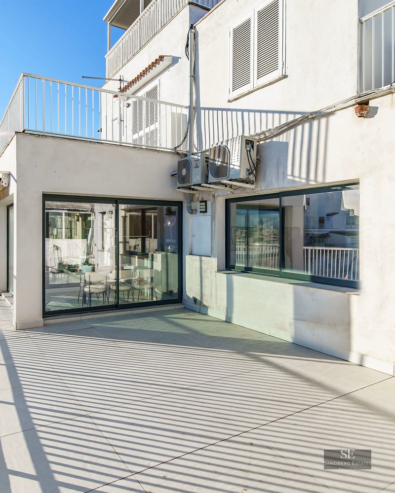Sunny terrace with light tiling, white railings, and a view of a city street under a clear blue sky.