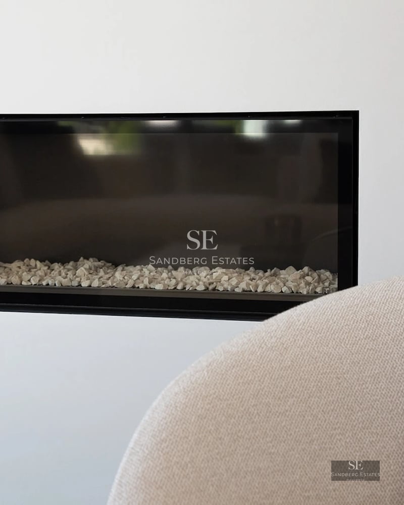 Close-up of a sleek black-framed horizontal fireplace with white stones, set into a clean white wall.