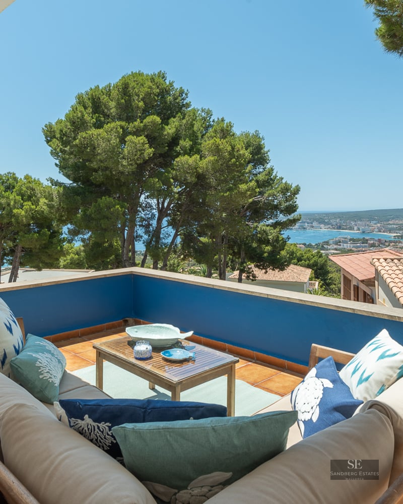 Outdoor terrace with L-shaped sofa, blue walls, and panoramic views of the Mediterranean coastline.
