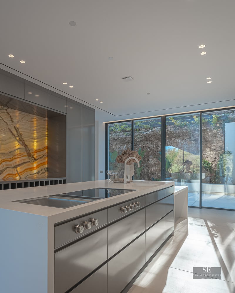 Modern minimalist kitchen with large island, sleek grey cabinetry, and a stunning backlit golden marble feature wall.