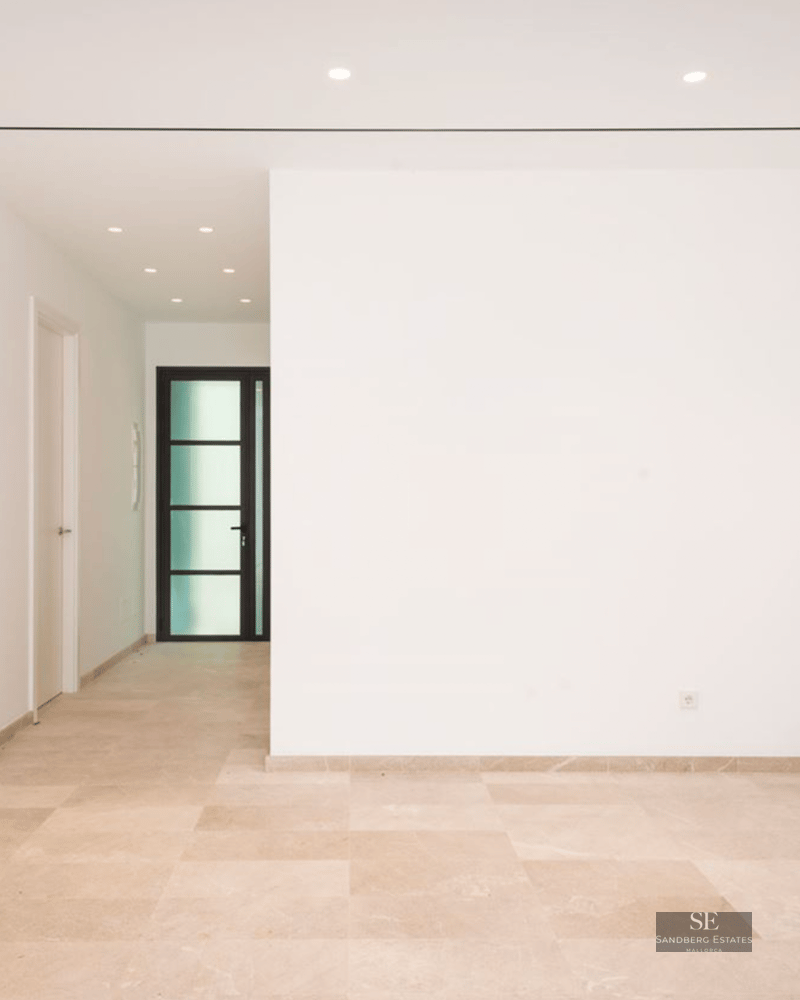 A bright, empty minimalist entrance hall with polished cream marble floors, white walls, and recessed ceiling lighting.