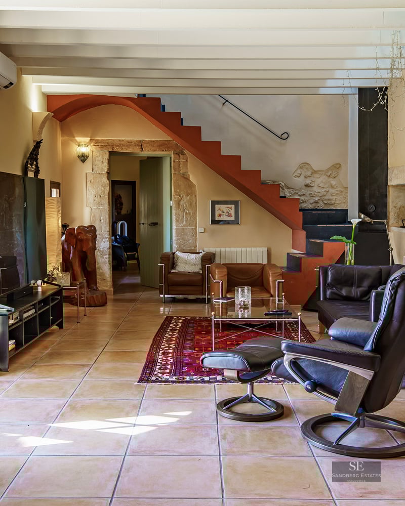 Sun-drenched living room with natural stone walls, terracotta tiles, exposed beams, and leather lounge chairs.