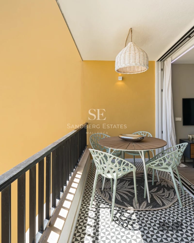 Bright living room with large windows and balcony overlooking the sea. Modern design, light wood floors, and minimalist furniture.