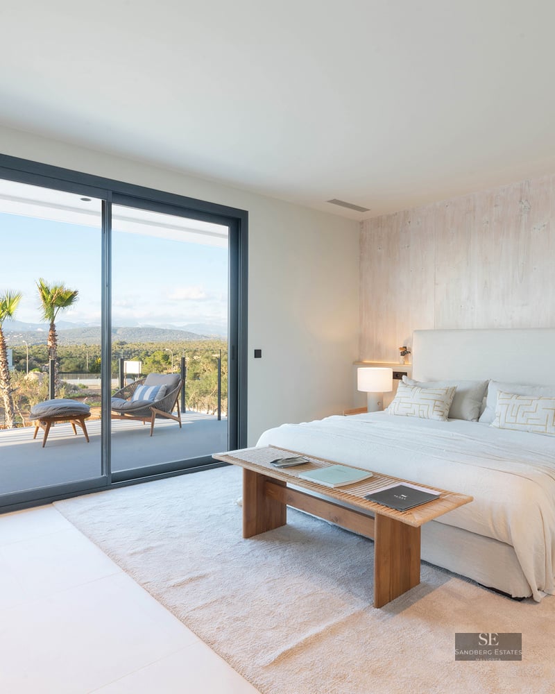 Luxury bedroom with white bed, wood accent wall, and glass door opening to a terrace with mountain views.