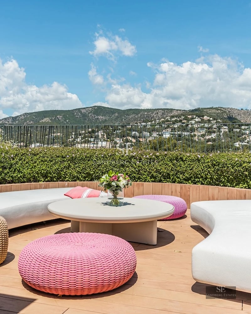 View of an infinity pool bordered by lawn and a modern villa featuring large windows and elegant outdoor furniture.