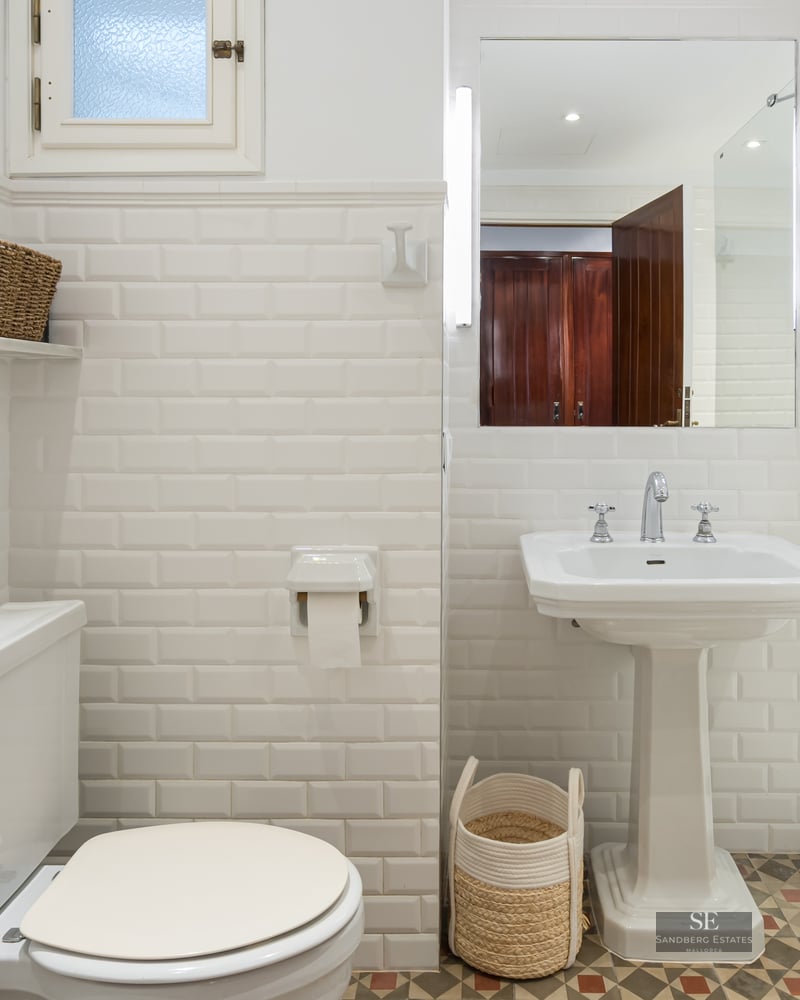 Bright bathroom with white subway tiles, pedestal sink, glass shower, and patterned floor tiles.