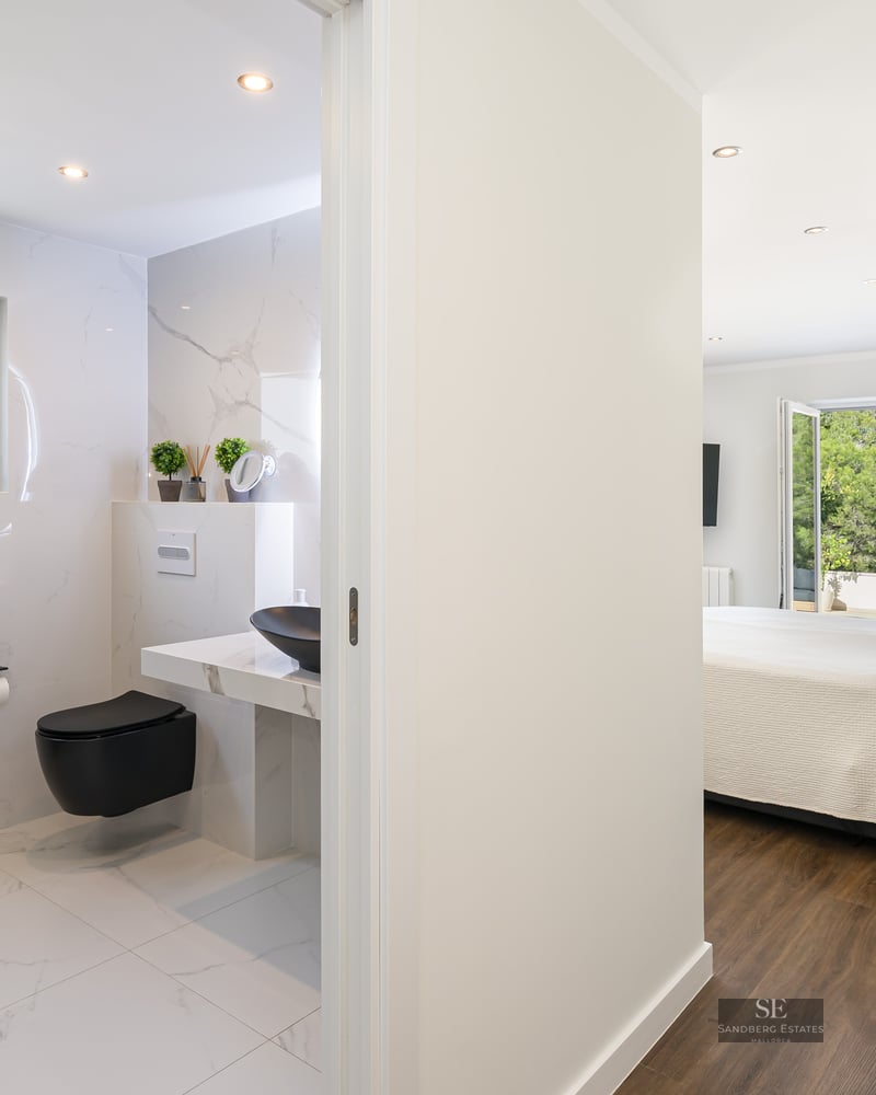 Chambre parentale lumineuse avec parquet et salle de bain moderne en marbre blanc et noir.