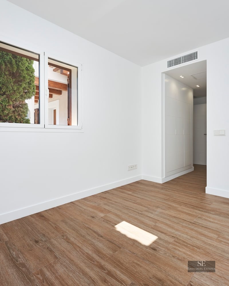 Empty room with white walls, wood-look flooring, a window, and a modern wall sconce.