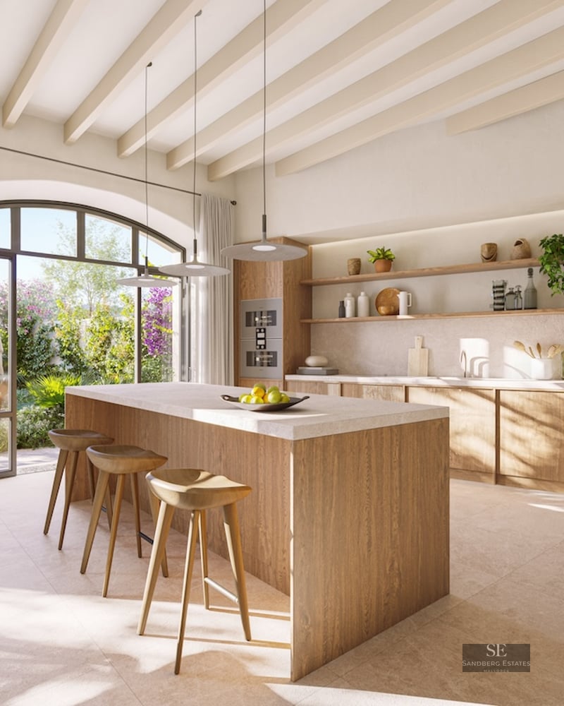 Bright kitchen with a large wooden island, three stools, and an arched glass door looking out to a lush green garden.
