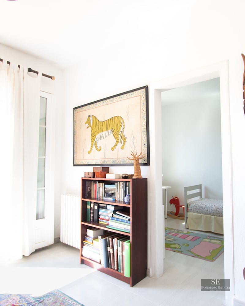 Bright interior with a bookshelf, tribal masks, and an open door leading to an outdoor swimming pool.