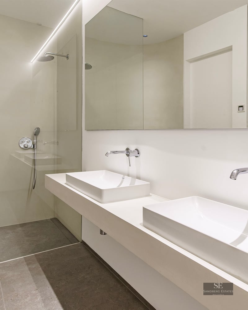 Modern bathroom featuring two white vessel sinks, wall-mounted chrome faucets, and a glass-enclosed walk-in shower.